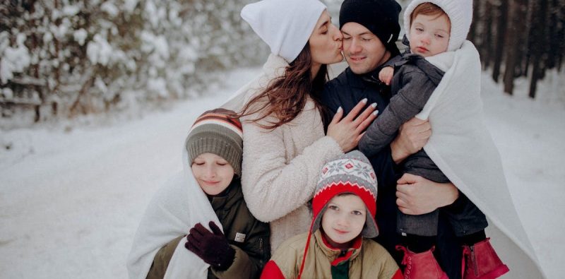A joyful family enjoying a snowy day in a forest, wrapped in warm clothing.