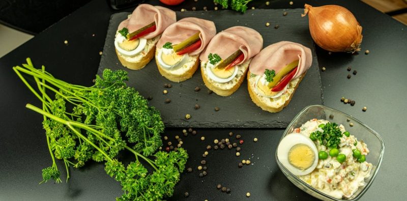 Delicious open-faced ham sandwiches with eggs, garnished with parsley, on a slate.